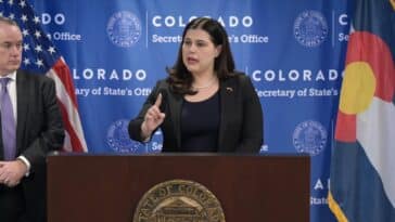 Colorado Secretary of State Jena Griswold speaks from behind a podium during a press conference.